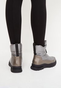 Bottines rembourrées argentées et grises avec une finition texturée, une boucle de traction et une semelle noire épaisse. Matériau supérieur doux pour la chaleur et le confort.