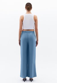 Lichtblauwe wijde broek met een elastische tailleband, gemaakt van een soepele stof. Draagt een witte cropped tanktop.