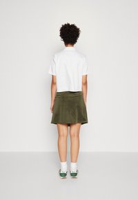 Chemise blanche à manches courtes, coupe courte, associée à une jupe en velours côtelé verte. Chaussures vertes Nike avec des chaussettes blanches.