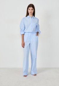 Camisa a rayas azul claro y pantalones a juego de tela suave; la camisa tiene un cierre frontal con botones y un único bolsillo en el pecho; ajuste relajado.