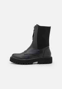 Botas negras hasta el tobillo con parte superior de cuero brillante y paneles laterales elásticos. Presentan un cierre lateral, suela resistente y un silueta robusta.