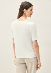 Hvid kortærmet t-shirt med rund halsudskæring og afslappet pasform, lavet af blødt stof. Bagfra viser den en sømløs skulderdesign.