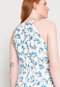 Vestido floral em branco com flores azuis e laranjas. Apresenta uma parte de trás franzida e design sem mangas, com um corte solto e tecido macio.