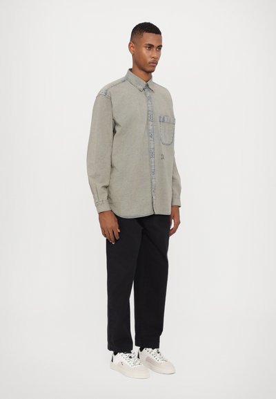 Grå långärmad skjorta med knappkrage, framficka och kontrasterande denimdetaljer. Buren med svarta byxor och vita sneakers.