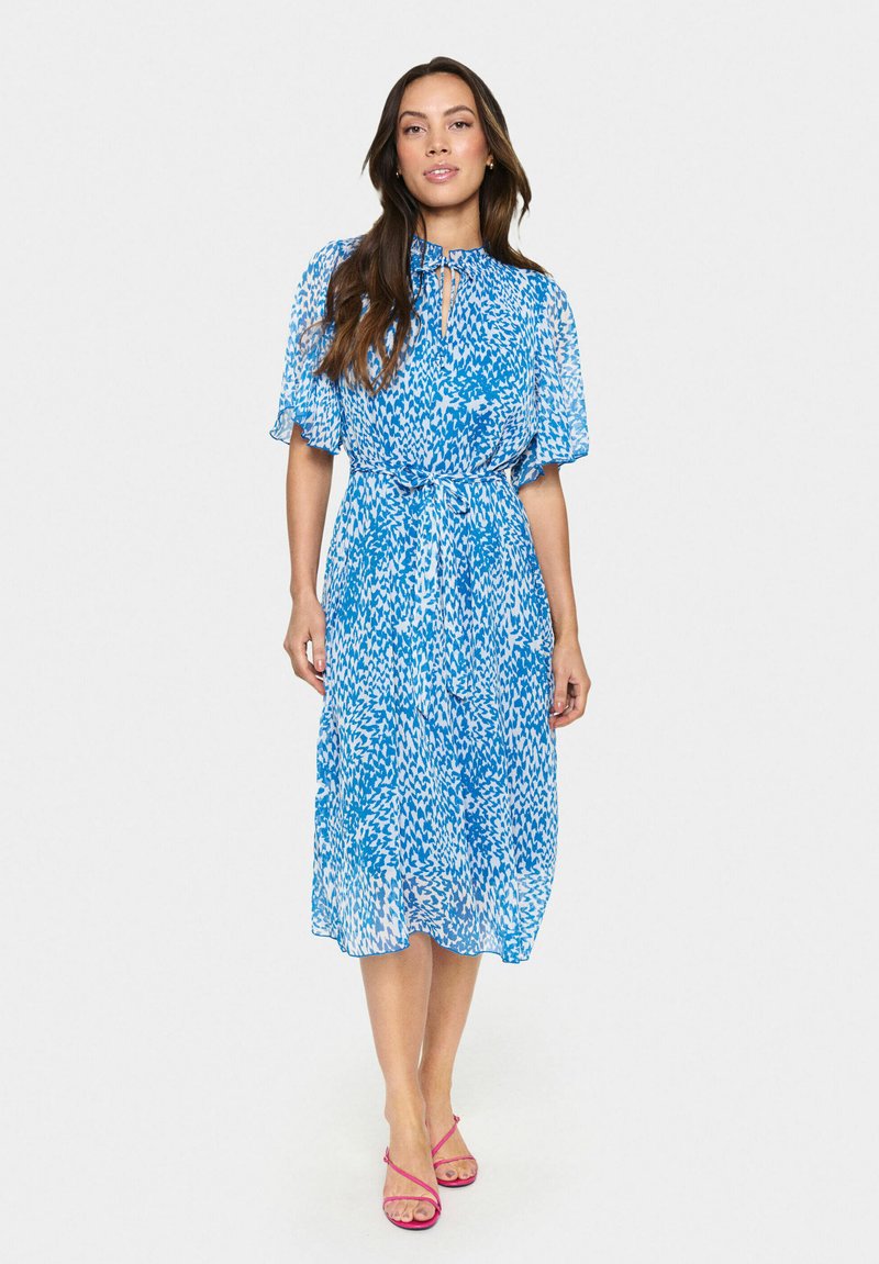 Robe midi imprimée bleue avec un détail de col noué, des manches courtes volantées et une taille cintrée. Tissu doux et fluide avec une texture légère.