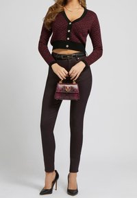 Burgundin lyhyt neuletakki, jossa on geometrinen kuvio, mustat reunat ja kolme nappia; yhdistettynä mustiin tiukkoihin housuihin ja mustiin korkokenkiin. Pieni kuvioitu käsilaukku.