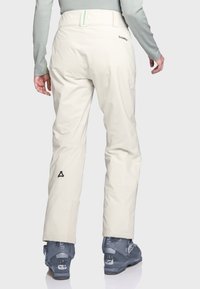 Beige Skihosen aus wasserabweisendem Material, mit hohem Taillenbund, Reißverschluss-Taschen hinten und Logodetail nahe dem Knöchel.