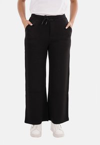 Pantaloni neri a gamba larga con vita regolabile, dotati di due tasche laterali rifinite con piccole borchie. Tessuto dalla texture liscia.