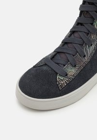 Zapatilla alta de ante gris oscuro, con acentos texturizados, patrón floral intrincado en el lateral y suela de goma gris.
