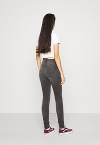 Vaqueros grises de talle alto con un corte ajustado, que cuentan con bolsillos traseros y un sutil ribeteado en las piernas, combinados con unas zapatillas rojas y blancas.