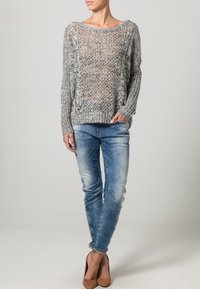 Maglione grigio chiaro a maglia con una vestibilità ampia, caratterizzato da un motivo testurizzato, abbinato a jeans skinny blu sfumati e tacchi marroni.