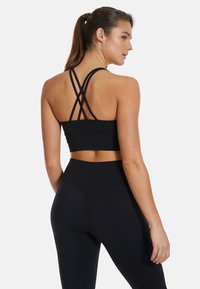 Black sports bra with crisscross straps and smooth texture. Paired with high-waisted black leggings featuring a snug fit and subtle seams.
