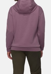 Lila hoodie med känguruficka, justerbar huva och ribbade ärmslut, i kombination med mörkgröna byxor. Logotyp sydd på baksidan.
