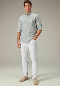 Hellblau-weiß gestreiftes Button-Down-Hemd, weiße Slim-Fit-Hose und beigefarbene Slipper mit Ausstanzungen.