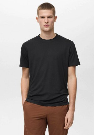 Maglietta nera a maniche corte realizzata in morbido tessuto, con scollo rotondo e vestibilità comoda. Indossata con pantaloni marroni, design minimalista.