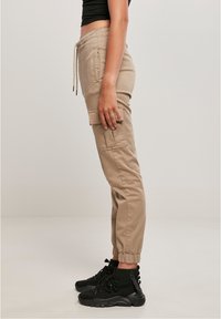 Beige cargo kalhoty s elastickým pasem, bočními kapsami a elastickými manžetami, spárované s černými kotníkovými botami. Hladká struktura tkaniny.