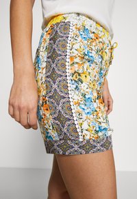 Květinové šortky v modré, oranžové a žluté barvě s jemným vzorem, elastickým pasem a dekoračním lemem podél švů.