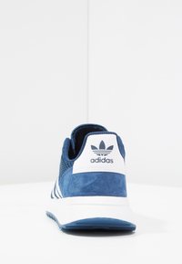 Modré semišové sportovní boty s bílými akcenty, jejichž svrchní část je z prodyšné síťoviny, design s třemi pruhy a označený pásek na patě.