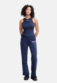 Canottiera a coste blu con logo, abbinata a pantaloni jogger blu, caratterizzata da una vestibilità rilassata. Il materiale appare morbido e confortevole, adatto per un abbigliamento casual.
