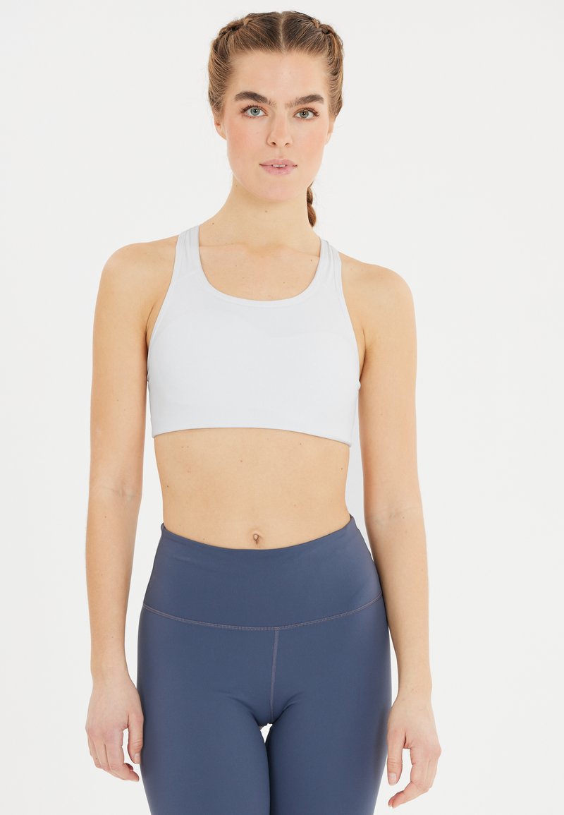 Ljust grå sportbh i mjukt material med racerback-design. Tillsammans med höga marinblå tights med subtila sömdetaljer.