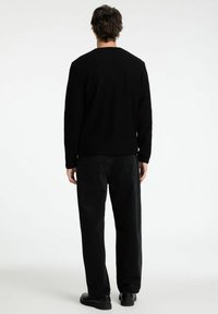 Must tumes, ümar kaelus, pikad varrukad, koos mustade teksadega. Materjal näeb välja pehme ja see on lõdva istumisega. Kingad on mustad.