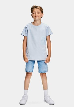 Lichtblauw katoenen T-shirt met korte mouwen, voorvak met "R" logo, gecombineerd met blauwe denim shorts en witte sneakers.