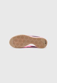 Semelle d'une chaussure Nike rose avec un motif hexagonal et un petit logo Nike noir près du talon sur fond blanc.