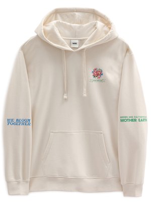 Person iført cremet hættetrøje med farverigt blomstermotiv og teksten "Fyldt med kærlighed, dyrket og plejet af Moder Jord" på ryggen.