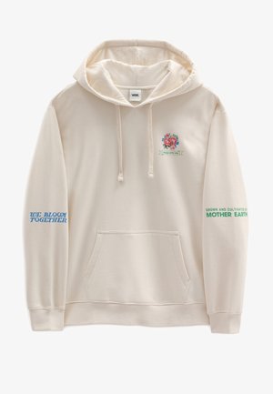 Persoon draagt een crèmekleurige hoodie met een kleurrijke bloemenprint en de tekst "Vol liefde verpakt, geteeld en verzorgd door Moeder Aarde" op de achterkant.
