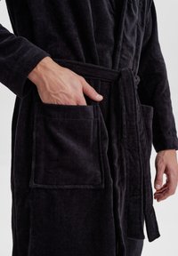 Schwarzer, strukturierten Bademantel mit einem Gürtel, der über zwei vordere Taschen verfügt. Der Stoff hat eine weiche, gerippte Optik.