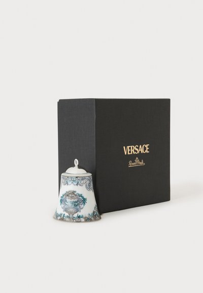 Clochette blanche décorative avec des motifs bleus et gris complexes à côté d'une boîte noire portant l'inscription Versace Rosenthal en lettres dorées.