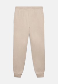 Pantalon de survêtement beige en coton doux. Il présente une taille élastique et des poignets effilés aux chevilles, avec une texture lisse et mate.