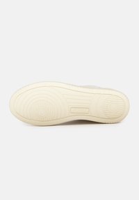 Suola di sneaker bianca in gomma testurizzata, con un motivo circolare e marchio. I bordi sono arrotondati, con una finitura liscia.