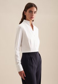 Witte geknoopte blouse met een getailleerde pasvorm, lange mouwen en knoopsluiting. Gepaard met donkere, op maat gemaakte hooggesneden broek.