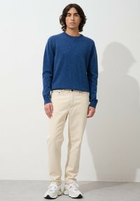 Pull en laine bleu, col rond, avec des poignets côtelés, associé à un jean beige clair et des baskets blanches. Design simple, texture lisse.