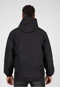 Giacca nera in nylon con cappuccio, polsini elasticizzati e orlo regolabile. Superficie testurizzata con una finitura liscia, adatta per un abbigliamento casual.