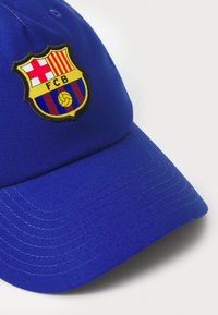 Casquette de baseball bleue avec une couronne structurée, arborant un logo brodé du FC Barcelone à l'avant, mettant en valeur des couleurs rouge, jaune et bleu.