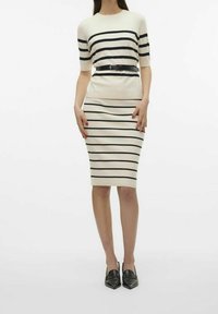 Pletené šaty s horizontálními černými pruhy na krémovém podkladu, s přiléhavým střih a černým opaskem v pase. Černé boty.