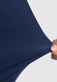 Tessuto elasticizzato marinato tirato per mostrare flessibilità e trama; superficie liscia ed uniforme senza motivi o decorazioni.