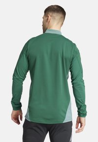 Maglietta sportiva a maniche lunghe di colore verde scuro con dettagli in azzurro chiaro, texture liscia e vestibilità regolare. Presenta un collo alto e cuciture piatte.