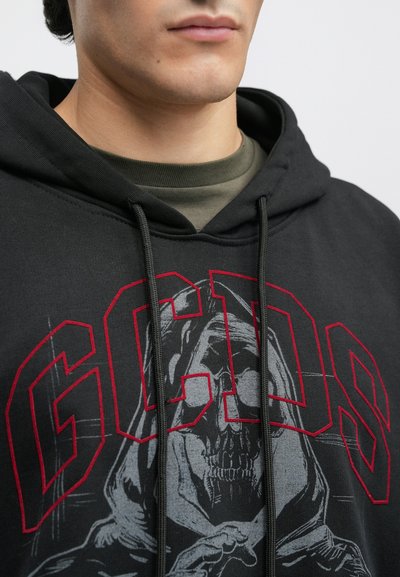 Hanorac negru cu text roșu "GCDS" și o grafică cu o figură cu glugă și un craniu. Sfoara de ajustare și o textură moale sunt vizibile.