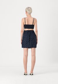 Conjunto de duas peças azul-marinho com um top cropped pregueado e uma saia a condizer, apresentando um padrão floral e alças finas ajustáveis.