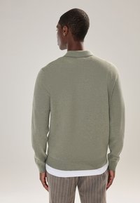 Lichtgroene gebreide trui met een kraag, geribbelde manchetten en een zoom. Draagt over een wit overhemd, gecombineerd met gestreepte broek.