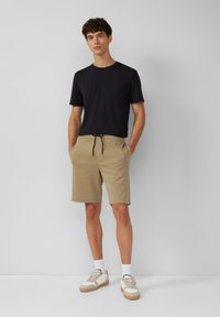 T-shirt noir à col rond, shorts beiges avec cordon de serrage et baskets légères. Tenue décontractée au design simple et aux textures douces.