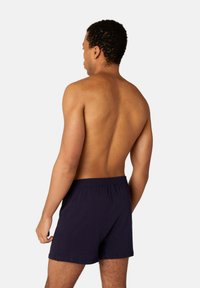 Navy blue cotton shorts with an elastic waistband, mid-thigh length, and a relaxed fit, shown from a back view.