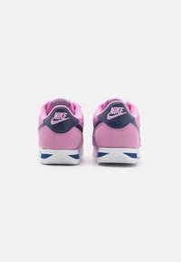 Rózsaszín velúrból és hálós anyagból készült Nike sportcipők, navy kiegészítővel, fehér középtalppal és mintás talppal. A sarkon és a nyelven logó található.