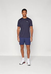 Meeste sportlik komplekt, millel on tumesinine lühikeste varrukatega särk ja sobivad lühikesed püksid, millel on valge logo. Tekstuuriga kangas ja minimalistlik disain.