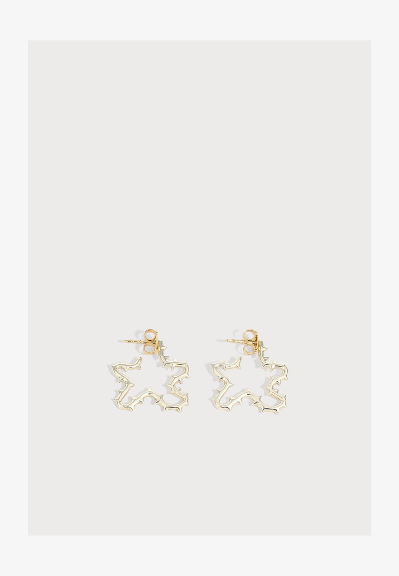 Paire de boucles d'oreilles clous en métal doré en formes abstraites et irrégulières d'éclats d'étoiles sur fond blanc.