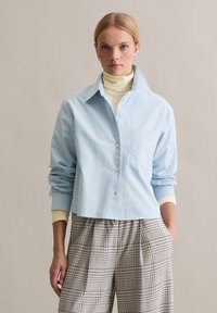 Helesinine nööpidega särk krae, ühe rinnatasku ja rullitud varrukatega. Kanditud kreemika kaelusega sukaga ning sobitatud ruuduliste pükstega.