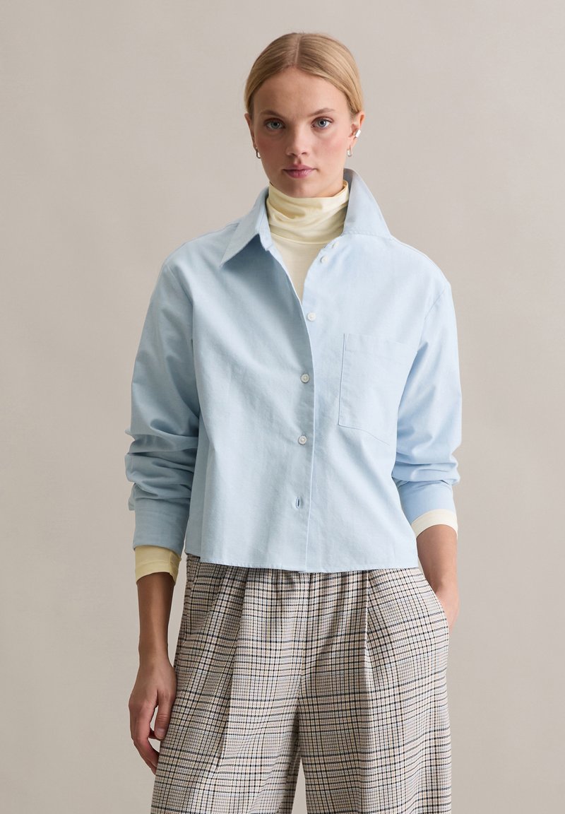 Helesinine nööpidega särk krae, ühe rinnatasku ja rullitud varrukatega. Kanditud kreemika kaelusega sukaga ning sobitatud ruuduliste pükstega.